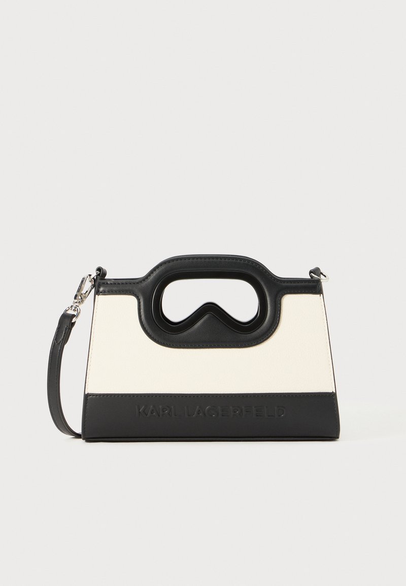 Konstrukcijas rokassomu ar matētu melnu un krēmbaltiņu krāsu kombināciju. Ievērojama izgriezta roktura iezīme un uzspiedušā zīmola nosaukums uz priekšpuses.