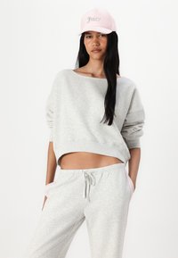 Sweat-shirt gris court à manches longues, associé à un jogging gris avec des bandes latérales roses, et une casquette rose avec "Juicy" en strass.