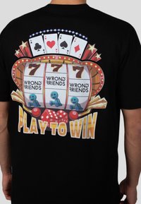 Camiseta negra con un gráfico colorido de una máquina tragaperras, dados y el texto "JUEGA PARA GANAR" en letra negrita.