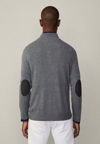 Pull en maille grise avec col, poignets côtelés et patchs noirs aux coudes, présentant un tissu texturé avec une coupe décontractée.