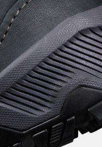 Nahaufnahme der schwarzen Schuhsohle mit strukturiertem Profilmuster und genähtem Obermaterial.