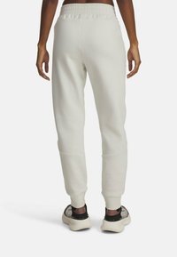 Light gray sweatpants with an elastic waistband and tapered cuffed ankles. Smooth texture with functional side seams. Worn with stylish sneakers.