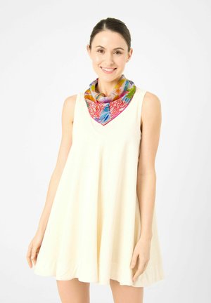 Smiling woman with dark hair wears sleeveless cream dress and colorful scarf with coral and sea life patterns against white background.