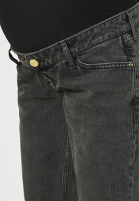 Mustat farkut ovat sileäpintaiset, kultaisella metallinapilla varustetut ja niissä on klassinen viiden taskun muotoilu. Kulutetut yksityiskohdat korostavat ilmettä.