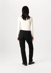 Jeans negros con un corte recto, combinados con una camiseta blanca de manga larga. Los jeans tienen bolsillos traseros mínimos y un diseño clásico.