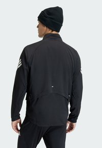 Black athletic jacket with a high collar, long sleeves, and reflective accents. Lightweight material, features a split back design.