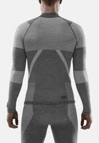 Maglia atletica grigia a maniche lunghe con pannelli testurizzati, design senza cuciture e taglio aderente. Include dettagli decorativi su spalle e maniche.