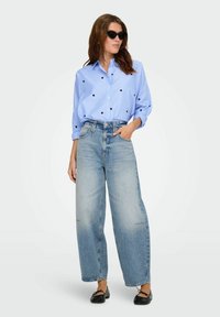 Camisa de cuadros azul de manga larga con patrones de corazones negros, combinada con jeans de pierna ancha de cintura alta y lavado claro, y zapatos de ballet negros.