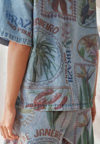 Tenue en denim comprenant un tissu bleu avec des motifs tropicaux vibrants, du texte incluant "Brésil, São Paulo", et un design décontracté.