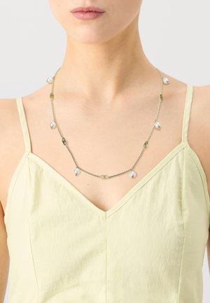 Gold chain necklace featuring irregularly placed white pearls and oval accents, displayed against a light yellow top.