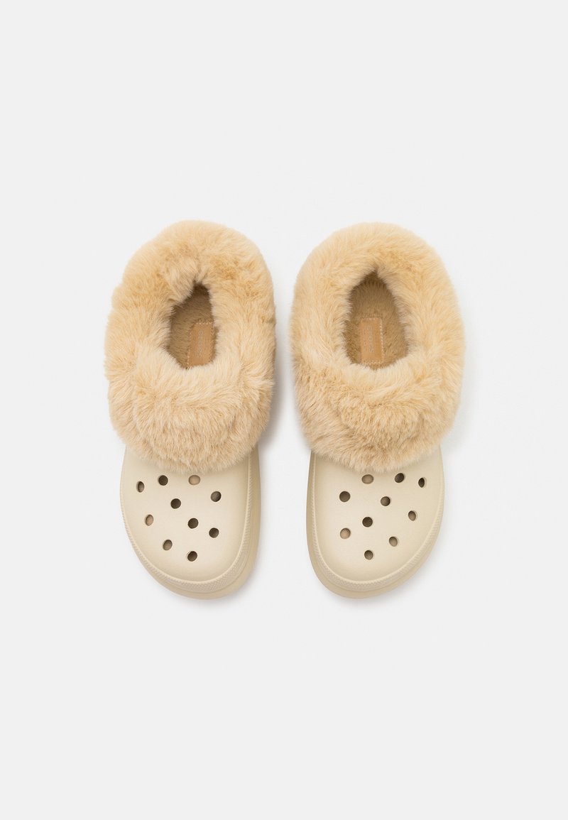 Zuecos beige con un suave forro de piel sintética beige, que presentan agujeros de ventilación y una suela plana. Superficie texturizada con un interior acolchado.