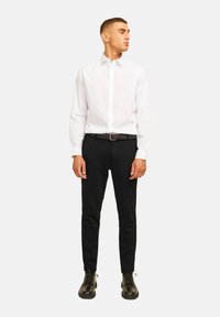 Camisa blanca de botones, pantalones negros y zapatos negros. La camisa cuenta con un cuello clásico, mangas largas y un diseño ajustado.