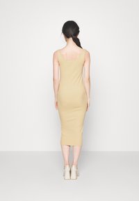 Pletené midi šaty těsně přiléhající k tělu v béžové barvě s výstřihem na zádech, s ramínky a hladkým povrchem, doplněné světlými robustními podpatky.