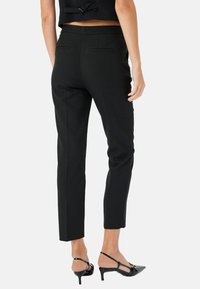 Pantaloni neri su misura con vestibilità slim, tasche laterali e tasche a filetto posteriori. Presentano una texture liscia e una lunghezza cropped. Abbinati a tacchi neri.