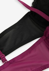 Twee beha's liggen plat: een zwarte met kant en een doorzichtig netwerk, en een rijke burgundy van glad, ondoorzichtig materiaal met een verstelbare band.