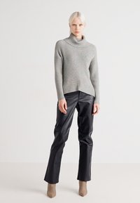 Pull à col roulé en tricot côtelé gris avec un col montant, associé à un pantalon droit en cuir noir et des bottines beiges.