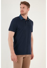 Námořnická modrá polo tričko s krátkým rukávem a džínsovým límcem. Má tříknoflíkovou légu. Hladká textilie, volný styl.