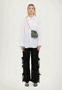 Λευκό υπερμεγέθες πουκάμισο με κουμπιά, μαύρο δαντελένιο παντελόνι με κορδόνια, μαύρη τσάντα μίνι με σχέδιο και αλυσίδα, και μαύρες γόβες.