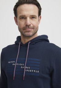 Sudadera azul marina con un estampado gráfico que incluye texto en blanco y azul, cordones ajustables con acentos rojos y una textura suave.