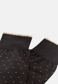 Guanti neri senza dita con pois bianchi, caratterizzati da una texture lavorata a maglia e polsini beige chiaro.