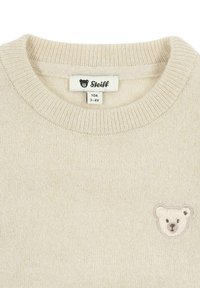 Beige gestrickter Pullover mit geripptem Kragen und kleinem Bärenstickerei auf der linken Brust. Das Etikett zeigt die Größe 3-4 Jahre und den Markennamen "Steiff."