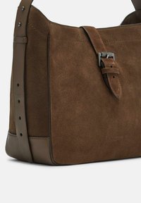Borsa a spalla in suede marrone con una forma strutturata, dotata di una base piatta, tracolla regolabile e dettaglio in metallo argentato.