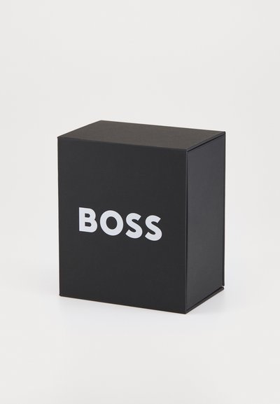 Черна правоъгълна кутия с матова повърхност, на която е изписана думата "BOSS" с дебел бял шрифт на предната страна. Прост и компактен дизайн.