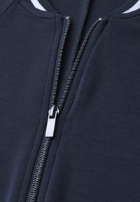 Close-up of a partially unzipped silver zipper on a navy blue fabric garment with white-striped collar detail.