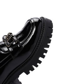 Zwarte patenten leren schoen met een chunky, gegroefd zool en decoratieve gespdetail op de bovenste band. Gladde textuur met een glanzende afwerking.