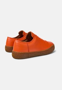 Orange leather sneakers with a textured brown rubber sole, featuring a rounded shape and lace-up design. Smooth surface with minimal stitching.