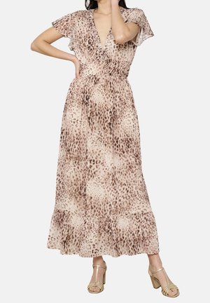 Kvinde iført en midi-længde leopardprint kjole med flagrende ærmer og gyldne højhælede sandaler, poserer med den ene hånd på hoften.