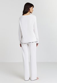 Haut à manches longues blanc et pantalon assorti en tissu texturé, avec des accents froncés noirs aux poignets et à l'ourlet, vu de dos.