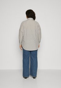 Striped, button-up shirt with a relaxed fit, featuring billowy sleeves and a curved hem, paired with wide-leg blue jeans.