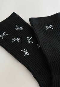 Schwarze gerippte Socken mit einem Muster aus Strass-besetzten Schleifen. Weiches Material mit strukturierter Stoffqualität, geeignet für den Freizeitgebrauch.