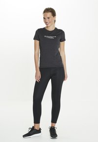 T-shirt de sport noir avec le logo "ENDURANCE" en blanc, associé à un legging noir ajusté et des baskets noires. Surface du tissu lisse, design léger.