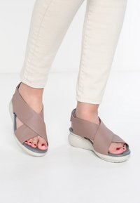 Sandali in pelle di un morbido mauve con cinturini incrociati, un accento grigio sulla suola e una piattaforma bianca spessa. Design open-toe.