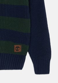 Blau- und grün gestreifter Pullover mit einem strukturierten Strickmuster. Verfügt über ein braunes Marken-Patch am unteren linken Rand und gerippte Bündchen.