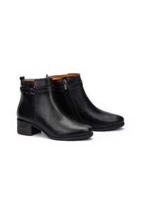 Botas de tobillo de cuero negro con un zipper lateral, forro marrón y un tacón bajo apilado. Presenta un acento de hebilla en la correa del tobillo.