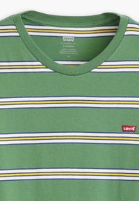 Žalias trumpas rankovės marškinėlis su horizontaliais baltais, geltonais ir mėlynais dryžiais, kairėje krūtinės pusėje esantis raudonas Levi's logotipas. Pagaminta iš medvilnės.