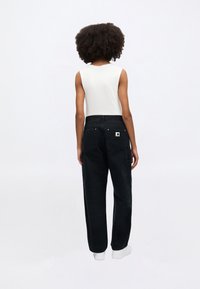 Μαύρο cargo παντελόνι με χαλαρή εφαρμογή, κατασκευασμένο από ανθεκτικό ύφασμα, με πλαϊνές και πίσω τσέπες, φορεμένο με λευκό αμάνικο τοπ.