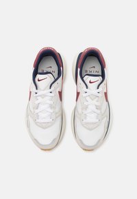 Bílé sportovní tenisky s červenými a tmavě modrými akcenty, s texturovaným svrškem, bílými tkaničkami a zaoblenou gumovou podrážkou.