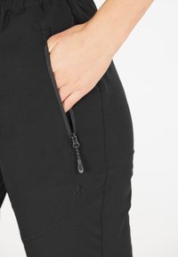 Svarta byxor med sidoficka med dragkedja, elastisk midja och subtilt texturerat mönster. Hållbart tyg med en slät yta.