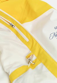 Giubbotto a vento giallo e bianco con tasca con zip, dettaglio a cordoncino e logo ricamato sulla parte bassa. Tessuto liscio e leggero.