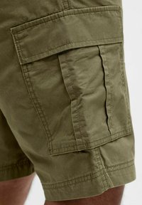 Olive green cargo shorts made of cotton, featuring side pockets, visible stitching, and a relaxed fit, with a textured fabric appearance.