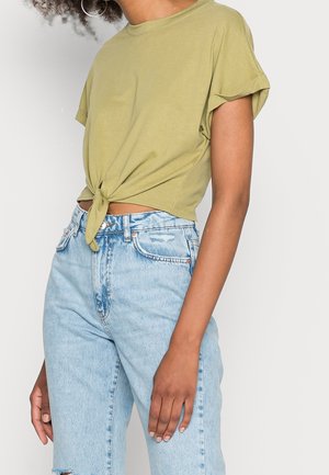 Camiseta de algodón de manga corta en verde oliva con detalle de nudo en la parte delantera, combinada con vaqueros de mezclilla azul claro desgastados y de tiro alto.