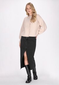 Lichtroze gebreide cardigan met textuur en knopen aan de voorkant, gecombineerd met een hoge taille zwarte denim rok met een split voor. Zwarte kniehoge laarzen.