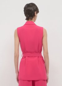 Blouse sans manches fuchsia avec col, taille ceinturée et design en couches de tissu. Texture lisse avec une silhouette classique et cintrée.