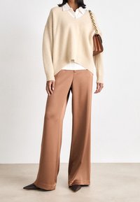 Beige oversized tröja, krämfärgad skjorta med krage under, matchad med lösa bruna satintrosor och spetsiga bruna klackar, tillsammans med en brun axelväska.