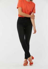 T-shirt rouge à manches courtes associé à un jean skinny noir taille haute et des sandales à talons ouvertes rouges avec un accent tressé.