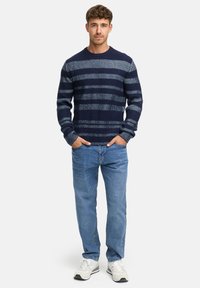 Marineblå stribet striktrøje med rund halsudskæring, struktureret stof og lange ærmer, parret med lyseblå jeans og hvide sneakers.